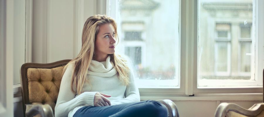 Mujer sentada cómodamente en un sillón en casa con una ventana al fondo