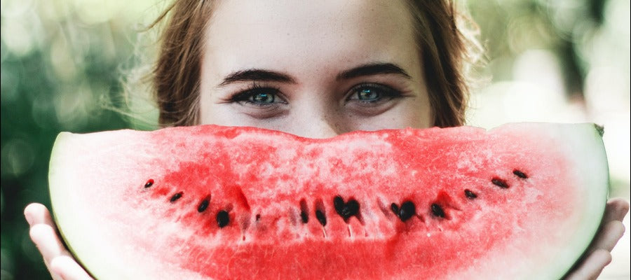 woman holding big watermelon slice in front of her face as a smile