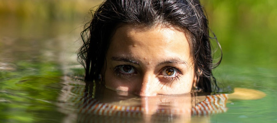 woman with face half submerged in the water outdoors with green reflections in the lake