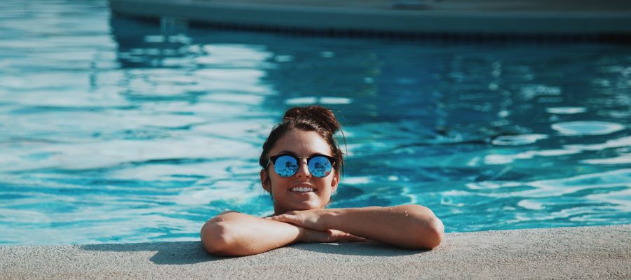 Mujer con gafas de sol apoyando la barbilla en las manos al lado de una piscina