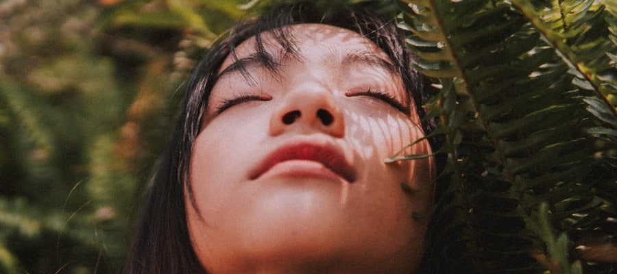 Asian woman with closed eyes and chin up surrounded by ferns