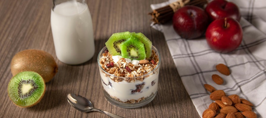 vaso con yogur probiótico con cereales, kiwis, almendras y manzanas rojas sobre mantel blanco