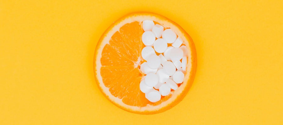 Naranja en rodajas medio cubierta con pastillas blancas de suplemento de vitamina C