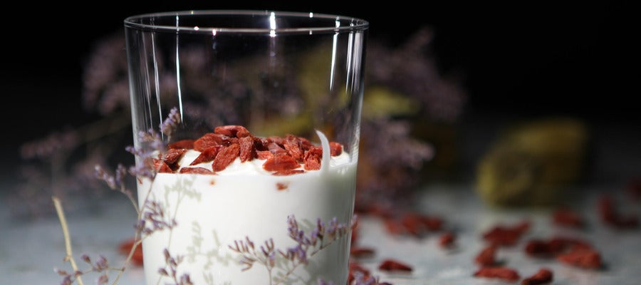 goji berries atop a glass of yogurt with goji berries and other plants in the background