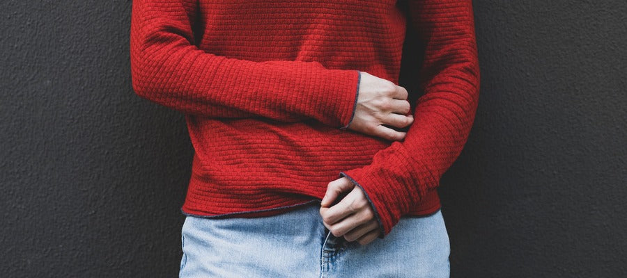 woman in red sweater and jeans holding one arm over stomach