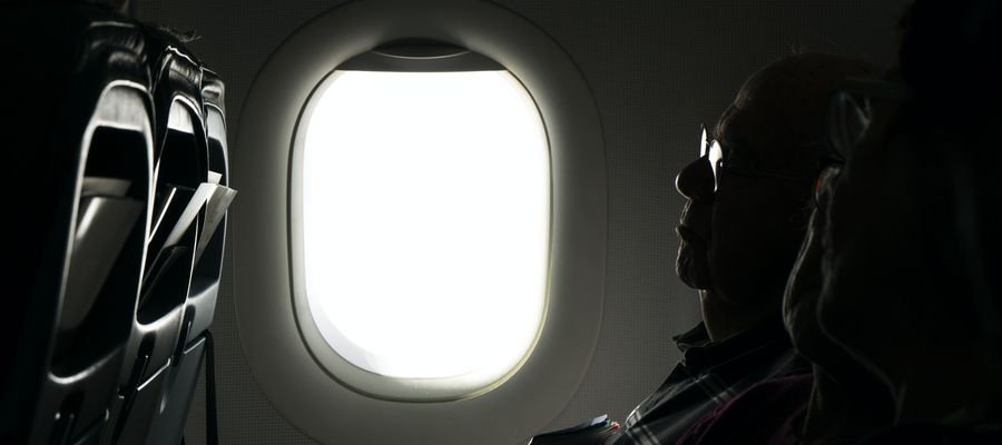 ventana de avión brillante con un hombre con gafas recostado en su silla en la oscuridad