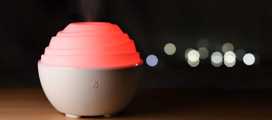 small round desk humidifier with red glow light on wooden table against blurry macro black background with lights