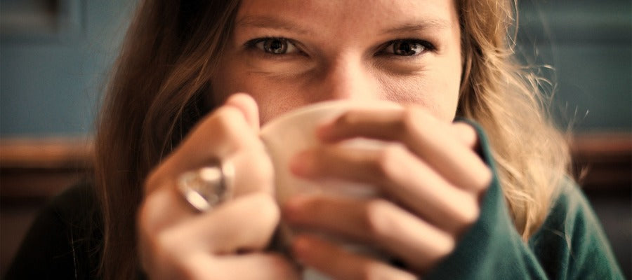 Primer plano de una mujer bebiendo de una taza con una expresión feliz en su rostro.