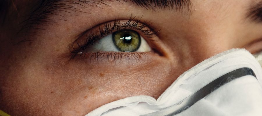 Primer plano del ojo verde del hombre con el borde de la mascarilla que cubre la nariz.