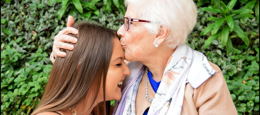 white haired woman with glasses and short hair kissing smiling young girl on the the forehead