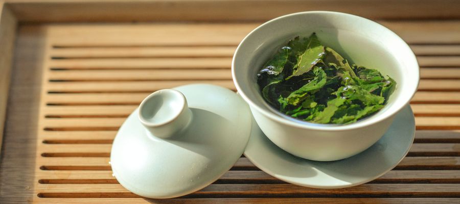 hojas de té en taza blanca colocadas en una bandeja de té de madera japonesa