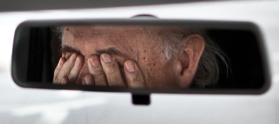old man rubbing eyes in car reflected on rearview mirror