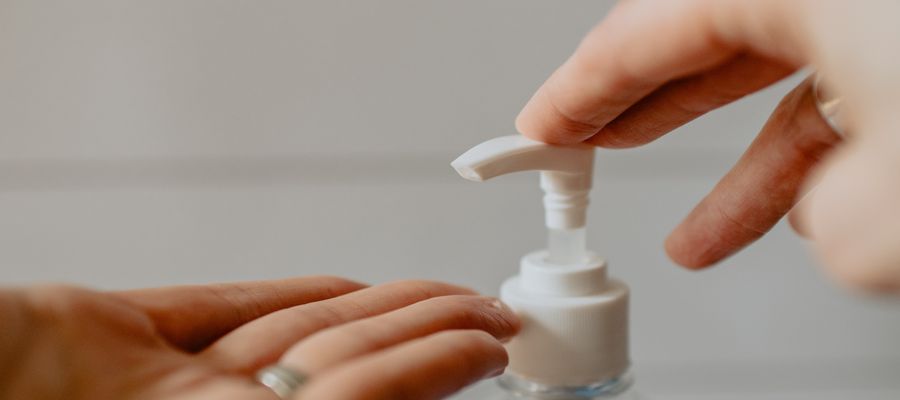 left palm held before liquid soup dispenser on which the other hand is about to push