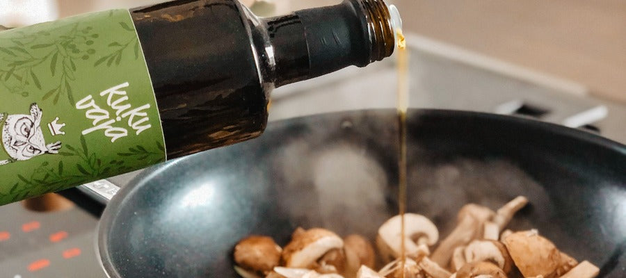 aceite de cocina vertido de una botella sobre champiñones en una sartén