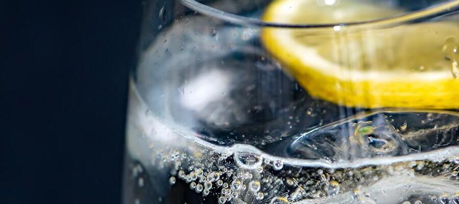 Primer plano de un vaso de agua transparente con cubitos de hielo y una rodaja de limón flotando en la superficie.