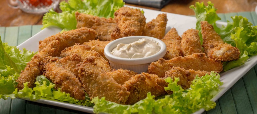 fried chicken nuggets on a square plate with a round dip in the middle and salad on the edges