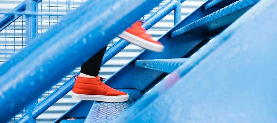 Persona con zapatos rojos subiendo escaleras de metal azul.