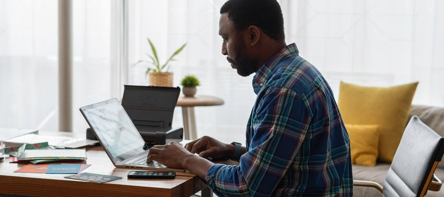 hombre sentado en un escritorio y trabajando en la computadora con la columna algo curvada