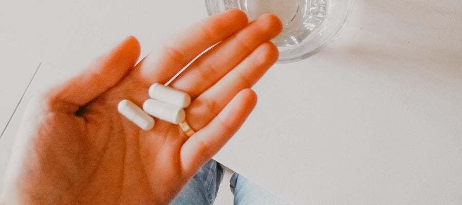 closeup of woman's hand with ring finger holding a few white capsules