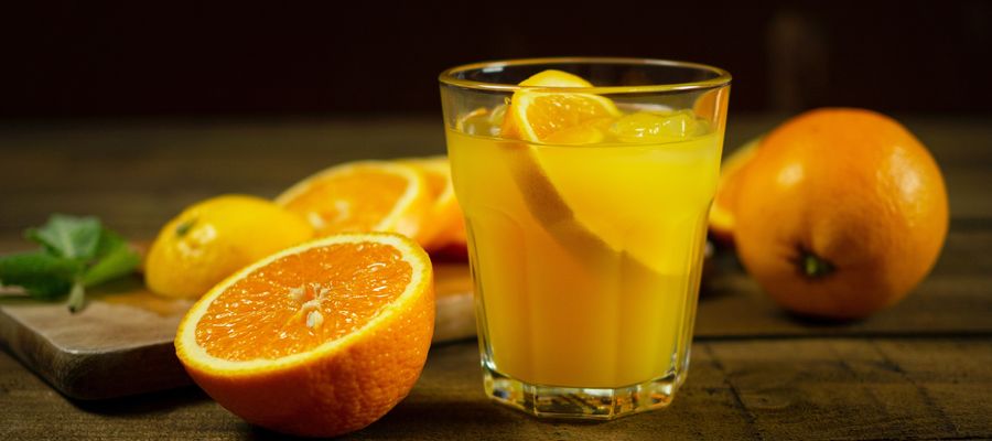 Jugo de naranja en un vaso con limones cortados sobre la mesa.