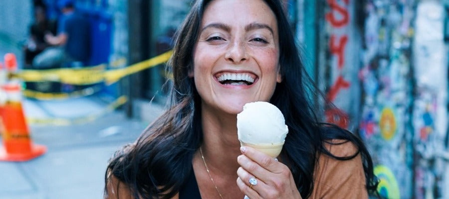 woman holding ice-cream cone in her left hand and smiling against blurry NY street background