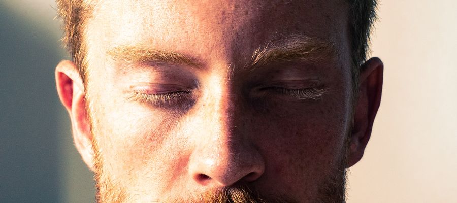 Rostro de un hombre con los ojos cerrados, medio iluminado y medio sombreado.