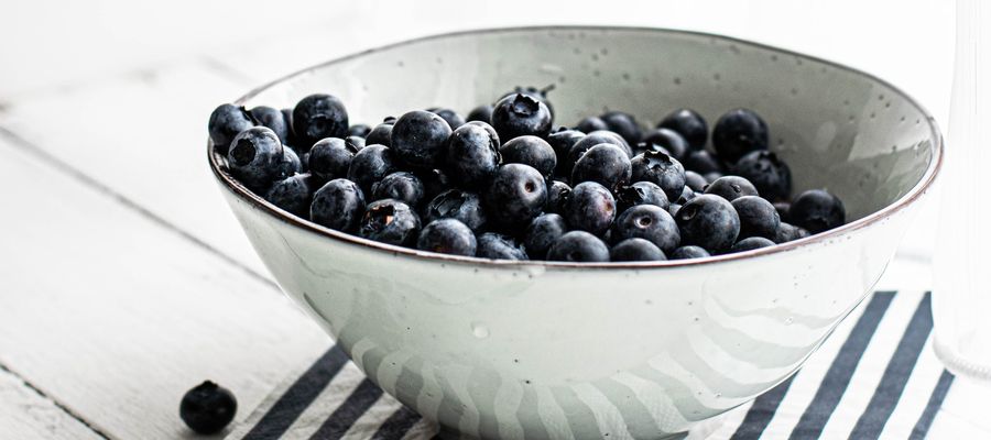 white bowl with blueberries on striped napkin set on white wooden table 