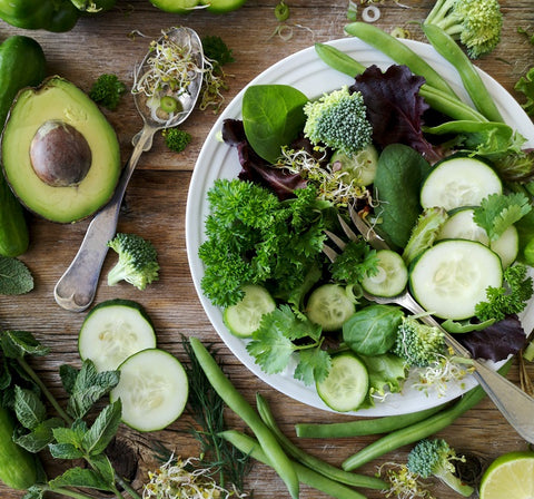 verduras de hojas verdes en un tazón blanco y sobre la mesa
