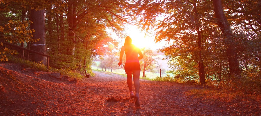 woman running on trail in the woods into twilight glow