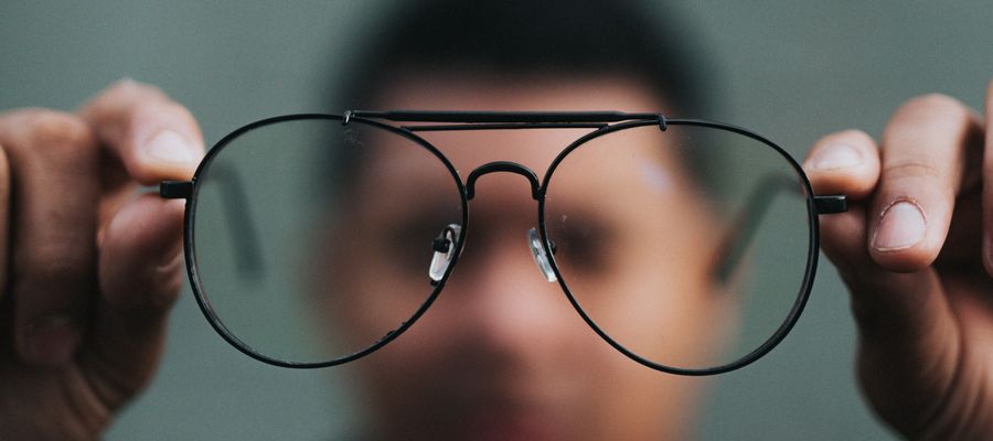 man holding pair of eye glasses in front with he is blurry in the background