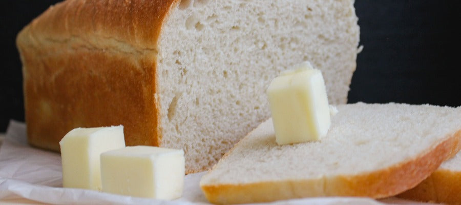 Rebanada de pan blanco con un cuadrado de mantequilla y una barra de pan blanco al fondo.