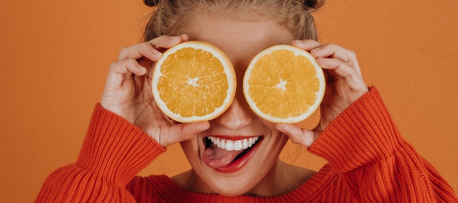 woman holding sliced oranges over her eyes against darker orange background