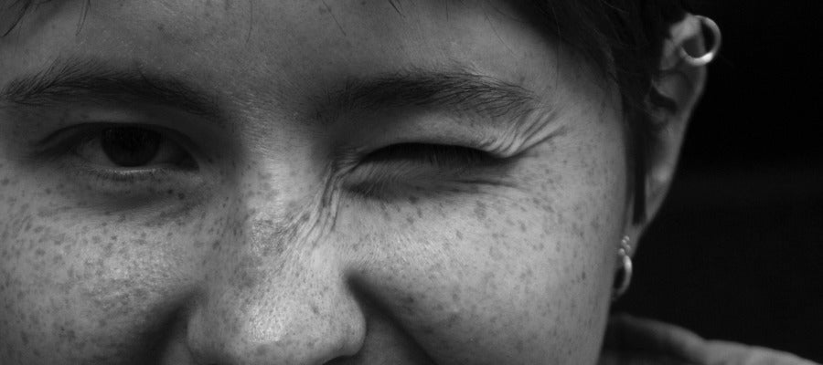 closeup of black and white portrait of woman with freckles blinking with one eye