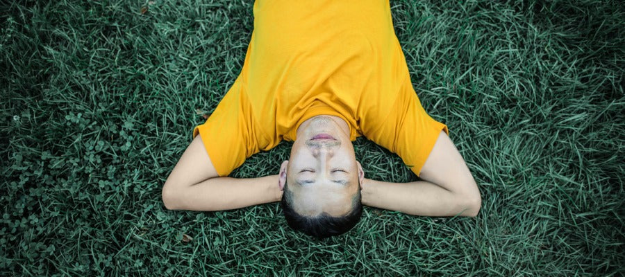 man in orange shirt lying on the grass with hands behind his head resting and relaxing