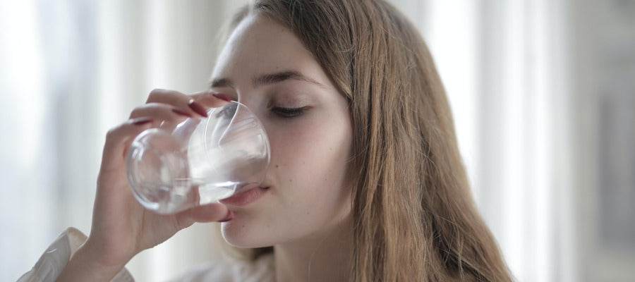 dehydrated young woman with long hair drinking water from a glass