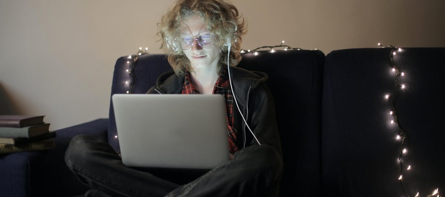 teenager using computer at night as he sits cross-legged on a dark couch