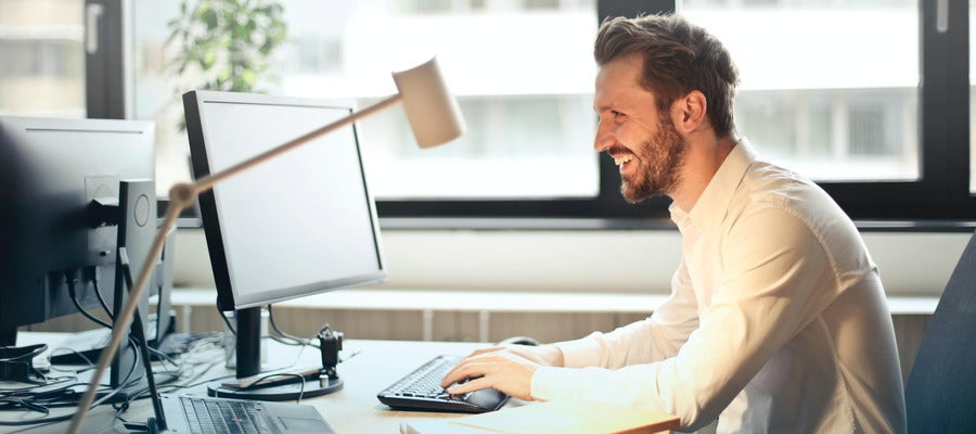 hombre sentado encorvado en su escritorio de oficina y sonriendo mientras trabaja en la computadora bajo una lámpara