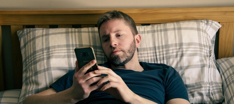 man lying in bed buttoning phone having eye strain