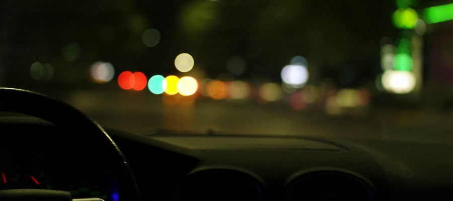 blurry street lights at night seen from the dark inside of a car with the wheel on the left