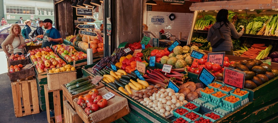 crates of colorful vegetables and fruits in a marketplace stall seen from an angle with people in the background