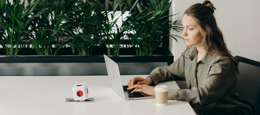 seated woman in green shirt working on a computer with green plants in the background