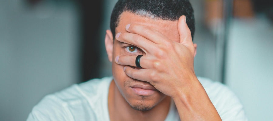 man in white shirt covering his face with his hand, showing only one brown eye