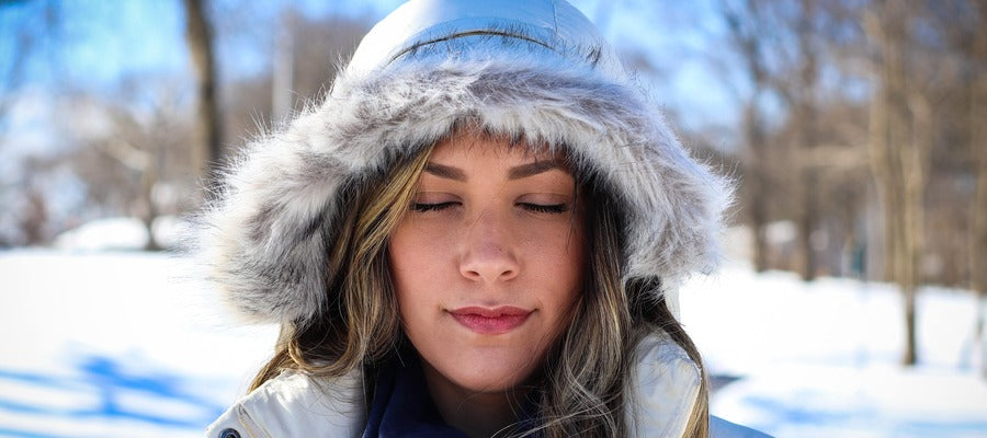 Mujer con capucha de piel con los ojos cerrados en un paisaje invernal con ojos secos