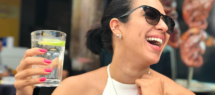 woman with sunglasses laughing while holding a glass of water in her right hand