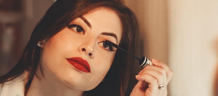 woman with red lips and eyeshadow applying makeup to her eyes
