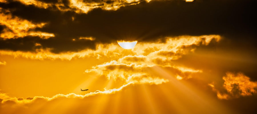 Estallido de sol amarillo anaranjado a través de las nubes al atardecer con nubes oscuras arriba y un avión volando a la luz