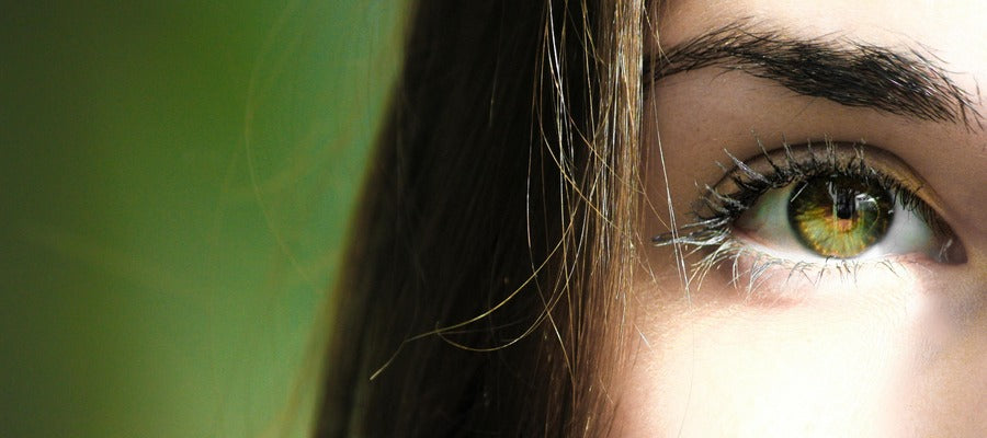 closeup of woman's green eye, eyebrow, and straight hair with lighted face against green background