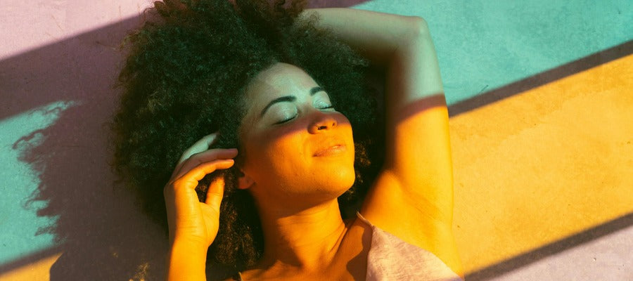 woman with Afro hairstyle lying back resting her eyes with colourful light strips washing over her