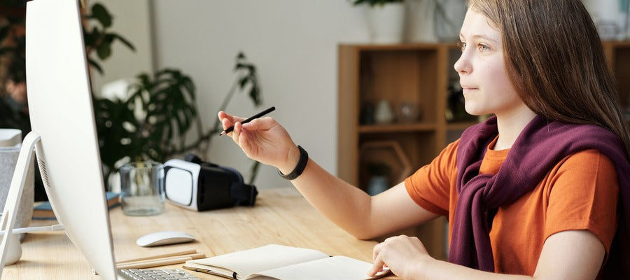 Adolescente con lápiz en una mano y cuaderno antes de estudiar frente a la pantalla de la computadora
