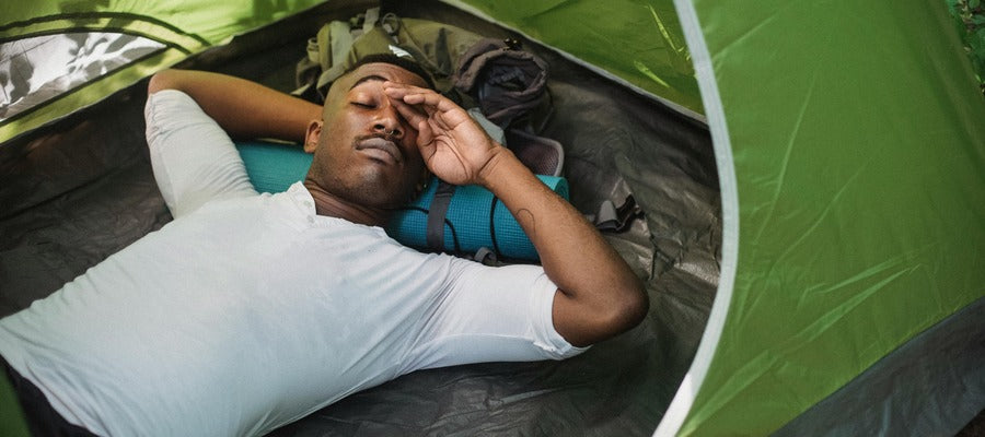African American man rubbing eyes while lying back in tent outdoors